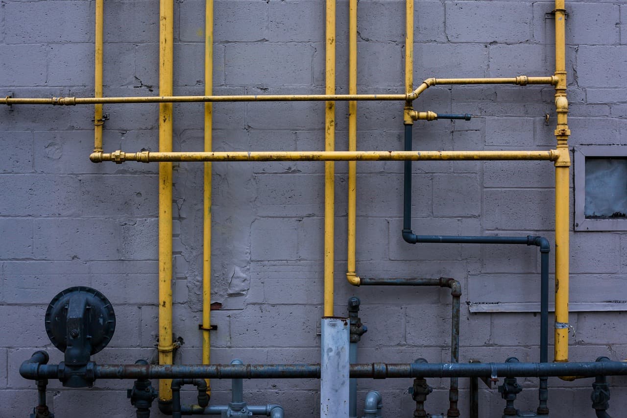 Yellow gas pipes run along a painted brick wall