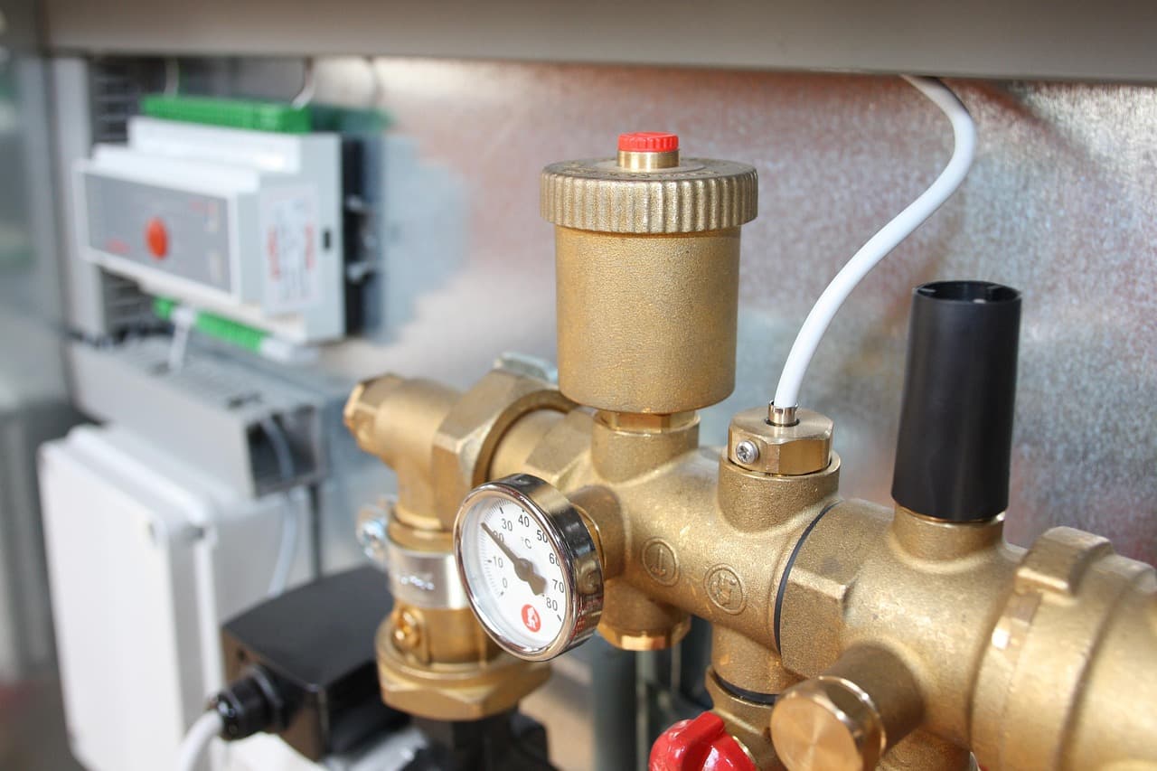 A brass pressure gauge and air vent on a heating manifold
